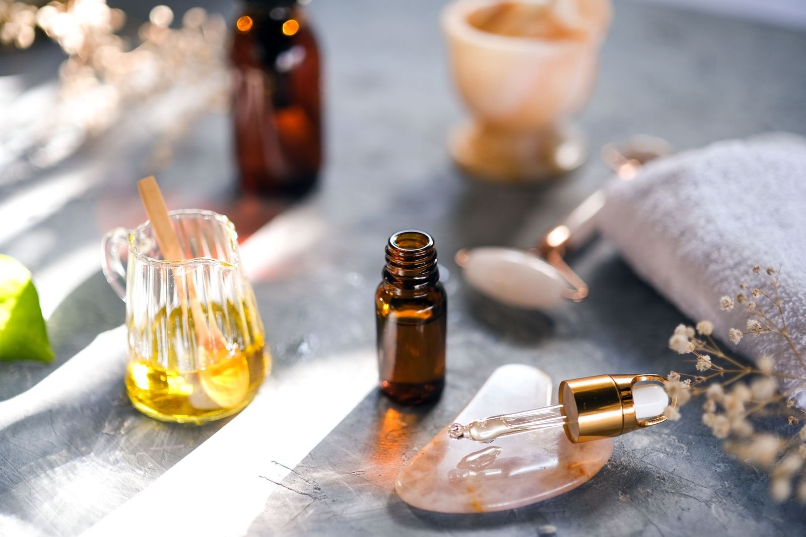 Small bottles of herbal oil and a glass jug of oil arranged on a stone surface