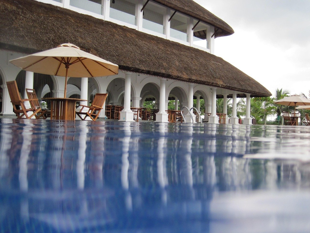 Blick über eine ruhige, grüne Gartenanlage eines gehobenen Ayurveda-Resorts mit Infinitypool und Liegen