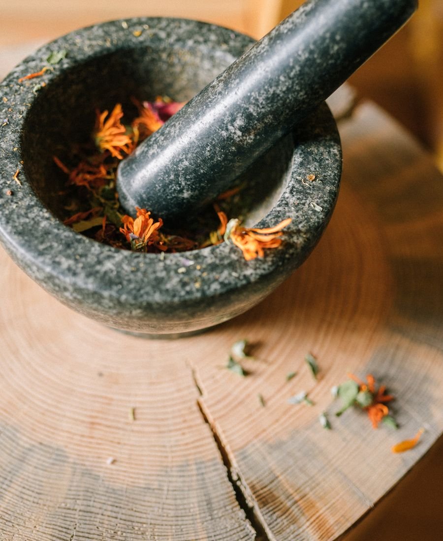 Stone mortar and pestle with dried herbs and flowers on a wooden board
