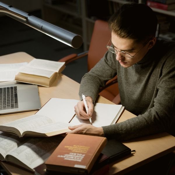 Student taking notes while reading textbooks at a desk