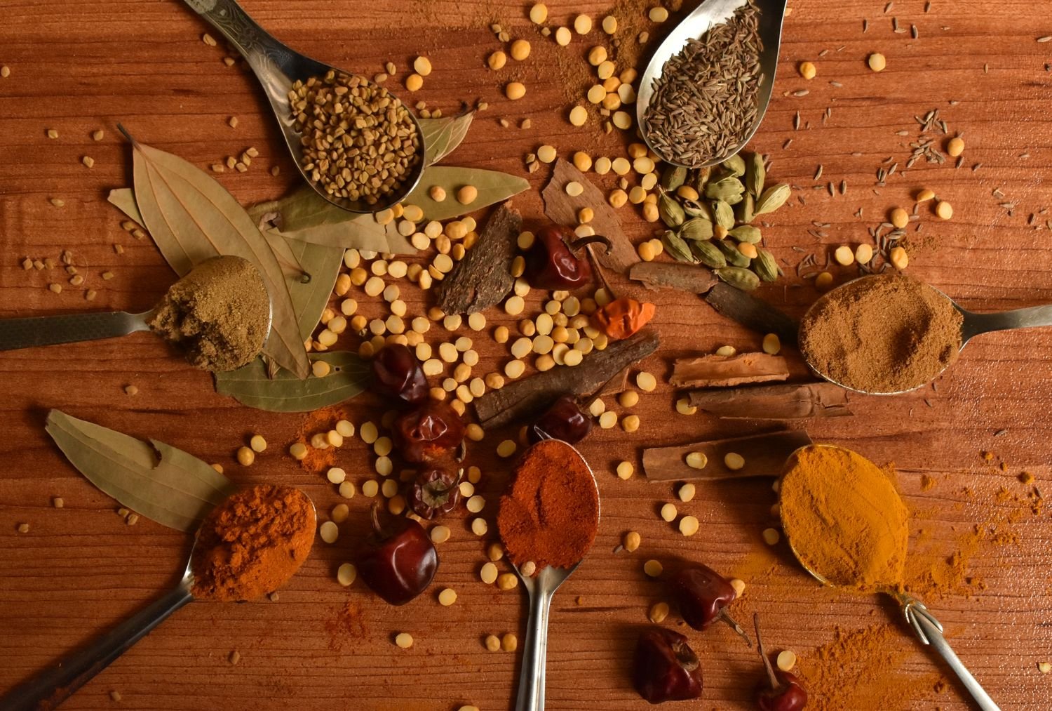 Indian spices including cumin, cardamom and turmeric arranged on wood