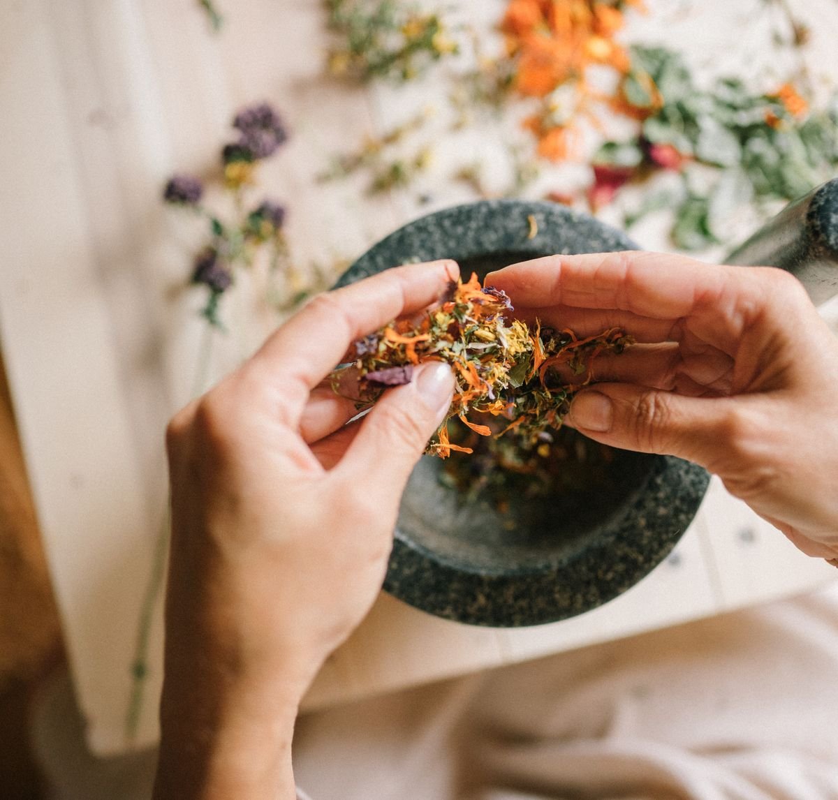 Hands preparing dried herbs in a stone mortar and pestle